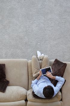 Man surfing on tablet on a couch at home, top view