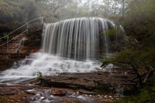 Beautiful perfect flows cascade over a misty Weeping Rock in Wentworth Falls, Australia