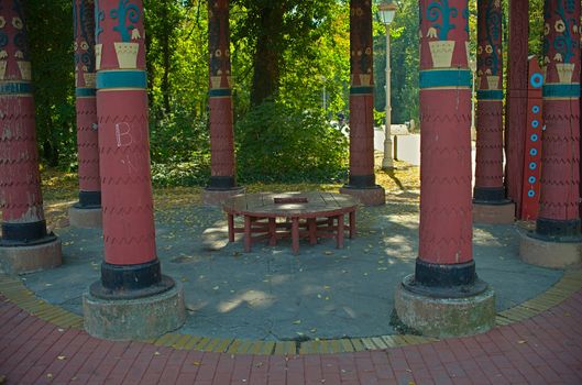 Red wooden round bench in a park surrounded by big red pillars