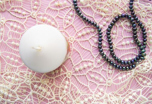 Flatlay pink background, graceful white expensive lace and elegant black pearl with candle, romantic style.