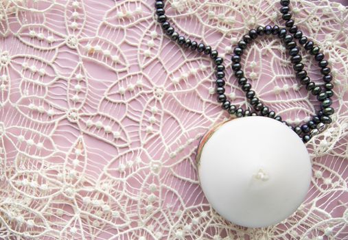 Flatlay pink background, graceful white expensive lace and elegant black pearl with candle, romantic style.