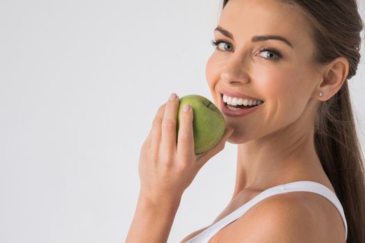 Young woman with healthy teeth smiling and biting green apple