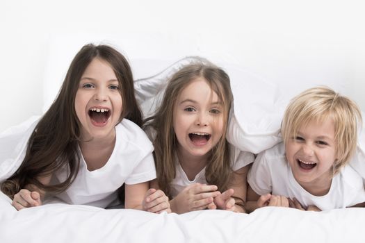 Happy three children under one blanket isolated on white background