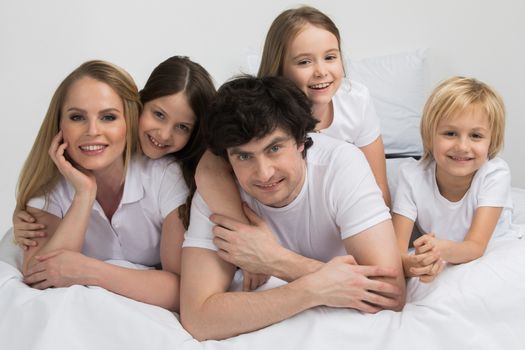 Happy smiling family of parents and three children together in bed