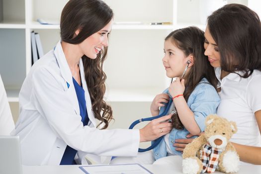 Young smiling female pediatrician doctor and her little patient with teddy bear