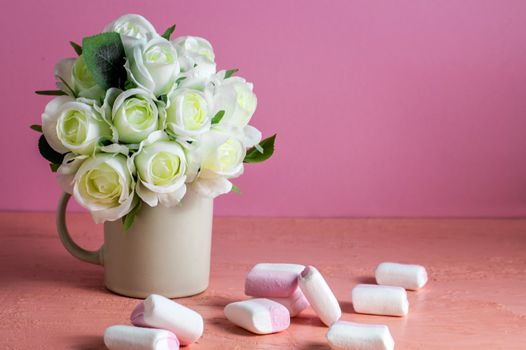 Copyspace with colorful mini marshmallows on a table next to white roses on a pink background