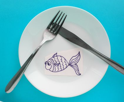 The celebration of April fool's Day, a Plate with a fork and knife and a paper fish on a blue background. Humor.