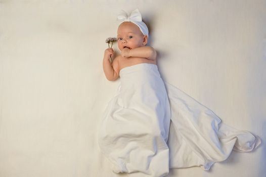 The baby girl with a bandage on his head holding a rose in his hand. The baby smiles.