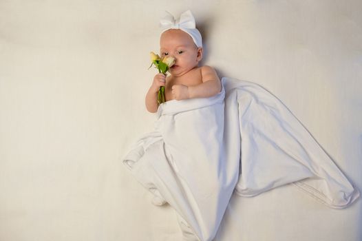 The baby girl with a bandage on his head holding a rose in his hand. The baby smiles.