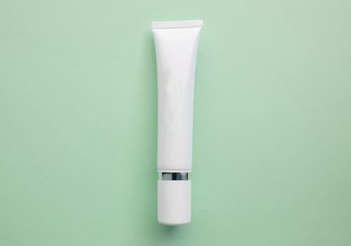 White plastic cream tube with space for text on a light green background, minimalism.