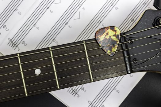 Guitar pick on fretboard with music note on black background.