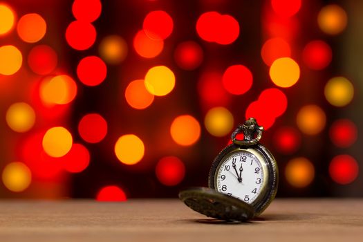 Closeup vintage old clock in the bokeh on brown wood background. The clock is near midnight. Concept Christmas and happy new year or everything related to time.