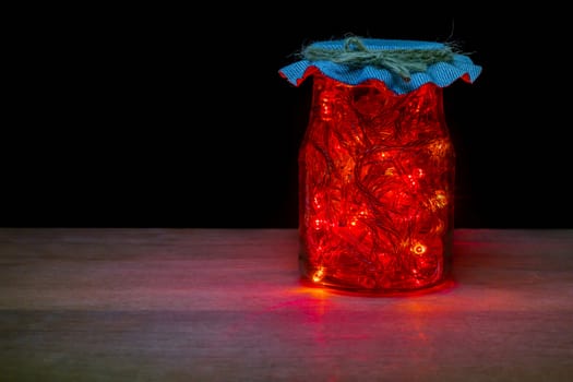 Red LED light in the glass bottle in darkness on brown wood table. Keep electrical energy for economical use. Concept of love the world and energy saving.