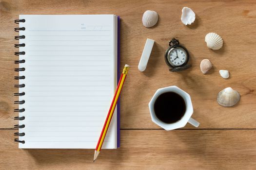 Bank notebook with pencil and eraser laying on the brown table. Vintage clock at 8 o’clock, Black coffee and shells on table.