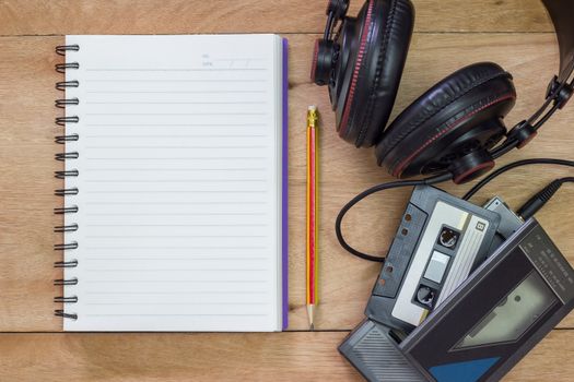 Bank notebook with pencil laying on the brown table. Vintage old tape player with headphones put on the table as well.