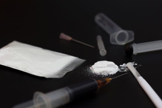 Fake Heroin or diacetylmorphine bag and syringes placed side by side. Low key addictive substance on darkness background.