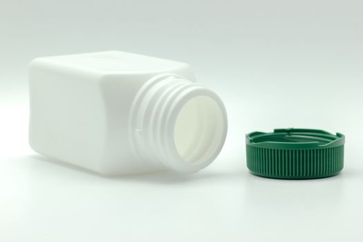 White bottle of antibiotic and green bottle cap placed on a white background.