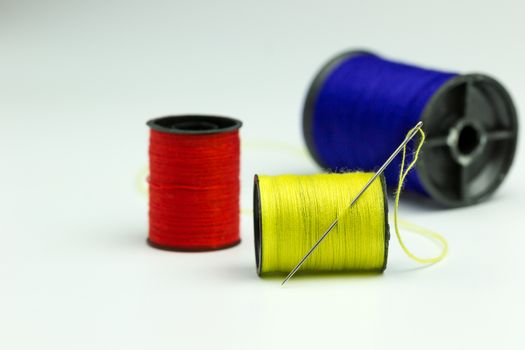 Close up Thread roller Blue, Red, Yellow and Sewing Needles in white background.Use to repair the tear of clothing.