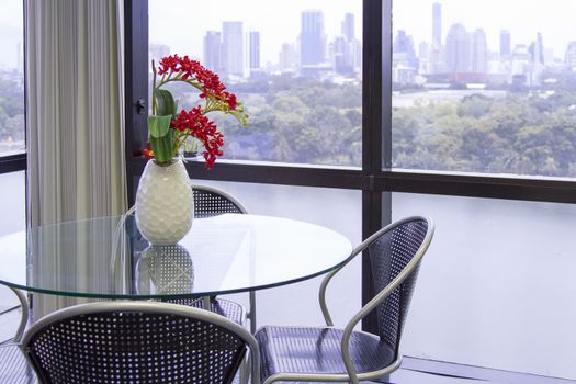 Round glass table with black chair with white vase, red flower on the building