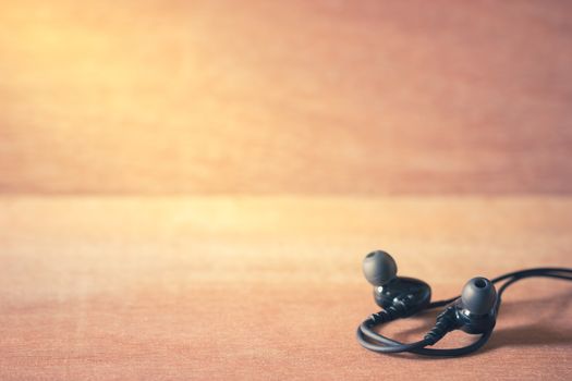 Closeup black In-ear monitor earphones on brown wood background in morning light.