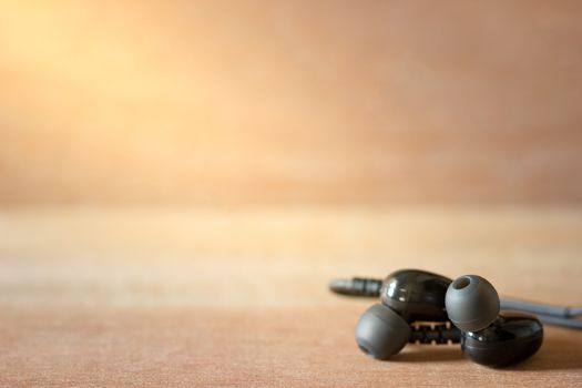 Closeup black In-ear monitor earphones on brown wood background in morning light.