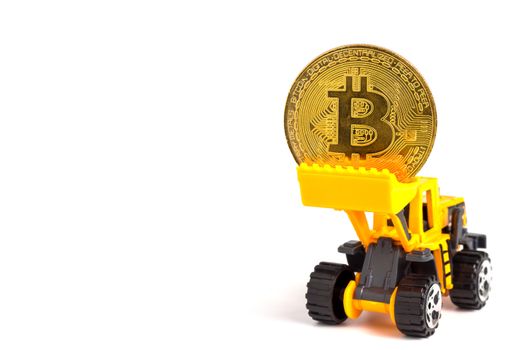 Close up yellow tractor model lifts up the golden coins. The concept of bitcoin mining business.