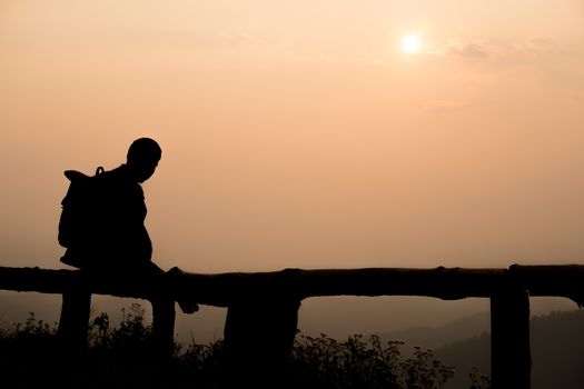 Silhouette lonely men sitting at the view point watching the sunset go down in among the mountains on evening.