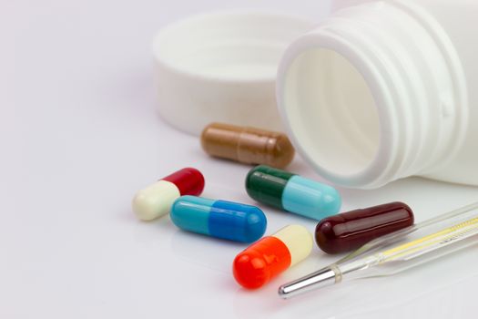 White pill bottle and colorful antibiotic capsule beside the thermometer