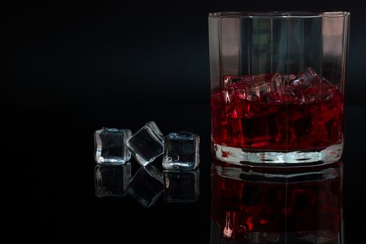 Polygon glass and reflection of liquor and ice on dark background.