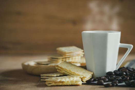 Crackers are placed on wooden plates and coffee cup with roasted coffee beans on a brown table.