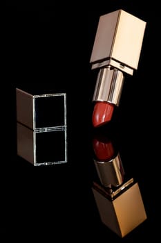Red lipstick in golden tube and reflection on dark background. Concepts of make up and beauty.