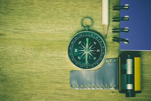 Compass photographic film and notebook with pencil placed on brown wooden table. The concept of tourism planning.