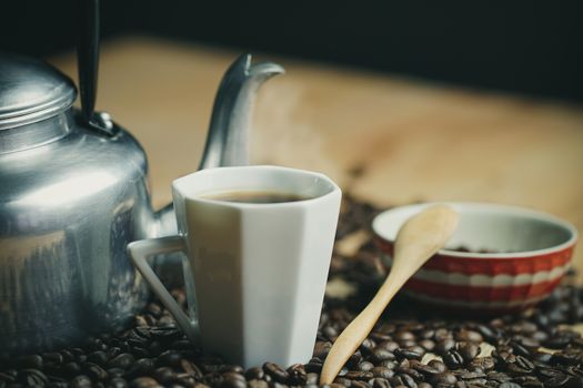 Coffee cup and hot pot. Roasted coffee beans on brown wood background in morning.