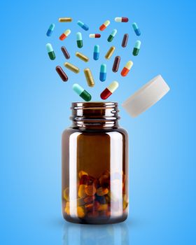 The medicine bottle is opened and the pill is floating in the shape of heart on blue background. Concept of health care.