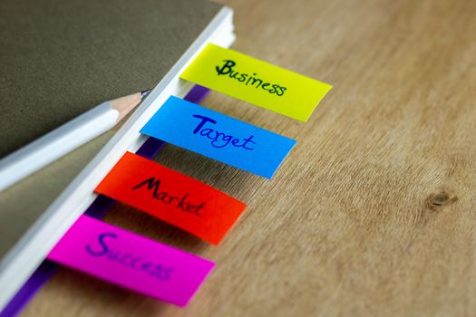 Colorful bookmarks are written for business, target, market, success, and have a white pencil put on a brown book cover. Concept of business.