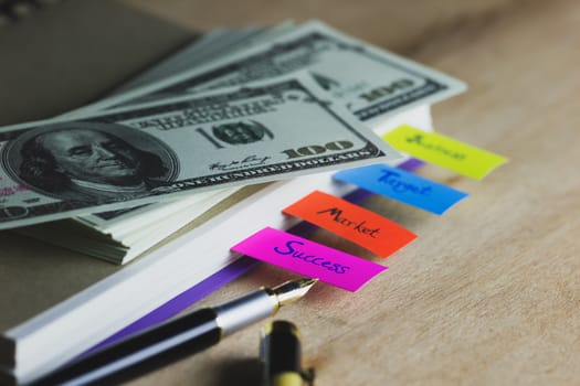 Business notebook and multicolour bookmark with banknote on wood table. Concept of business.