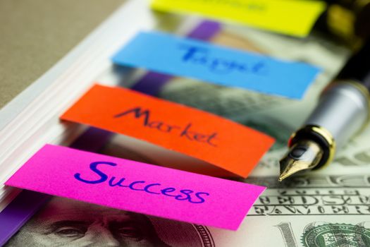 Business notebook and multicolour bookmark with banknote on wood table. Concept of business.