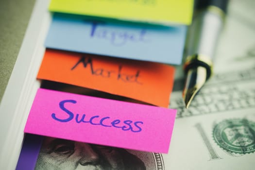 Closeup multicolour bookmark in business notebook and pen with banknote on wood table. Concept of business.