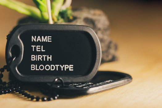 Soldier tag or dog tag laid on brown wooden table with stone and morning sunlight.