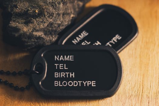 Soldier tag or dog tag laid on brown wooden table with stone and morning sunlight.