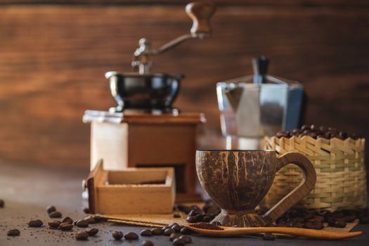 Brew black coffee in coconut cup and morning lighting. Roasted coffee beans in a bamboo basket and wooden spoon. Vintage coffee grinder and moka pot. Concept of coffee time in morning or start the new day.