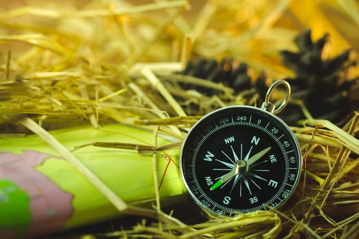 Compass with paper maps and pine flowers placed on dry wheat straw in morning sunlight. Concept of adventure tourism or survival in the forest.