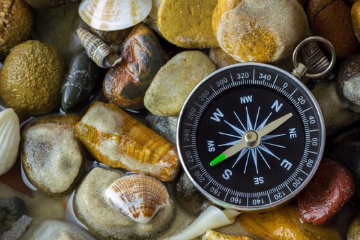 Compass on the pebbles and shell at riverside. Concepts of tourism and adventure.
