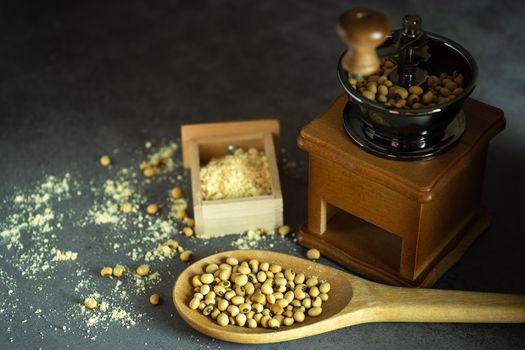 Coffee grinder grinding soybeans into powder and wooden ladle in darkness. Used to make soy milk.