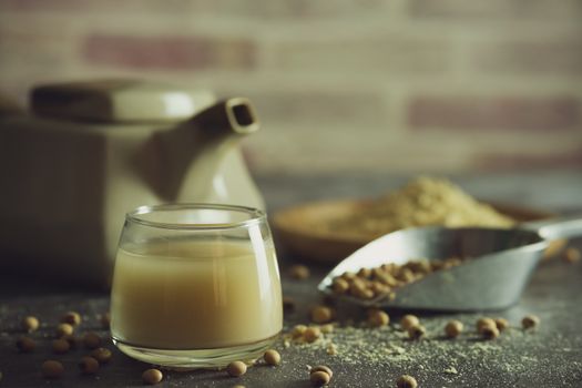 Soymilk in the glass and the kettle is placed beside. Soybean powder is crushed in a wooden dish and has scattered soy beans on the table in morning light.