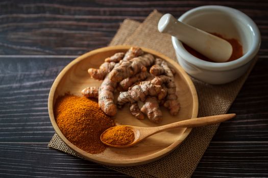 Turmeric powder and turmeric root on wooden dish with mortar and pestle on hemp mat in morning sunlight. Concepts of herbal medicine and health care.