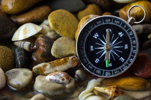 Compass on the pebbles and shell at riverside. Concepts of tourism and adventure.