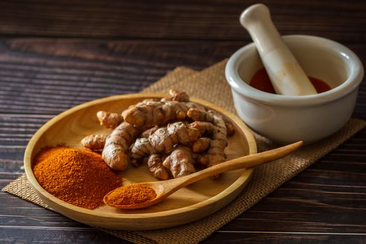 Turmeric powder and turmeric root on wooden dish with mortar and pestle on hemp mat in morning sunlight. Concepts of herbal medicine and health care.