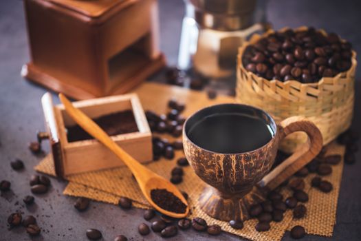 Brew black coffee in coconut cup and morning lighting. Roasted coffee beans in a bamboo basket and wooden spoon. Vintage coffee grinder and moka pot. Concept of coffee time in morning or start the new day.