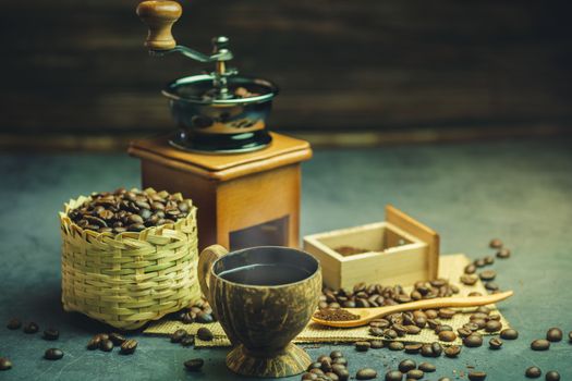 Brew black coffee in coconut cup and morning lighting. Roasted coffee beans in a bamboo basket and wooden spoon. Vintage coffee grinder and moka pot. Concept of coffee time in morning or start the new day.